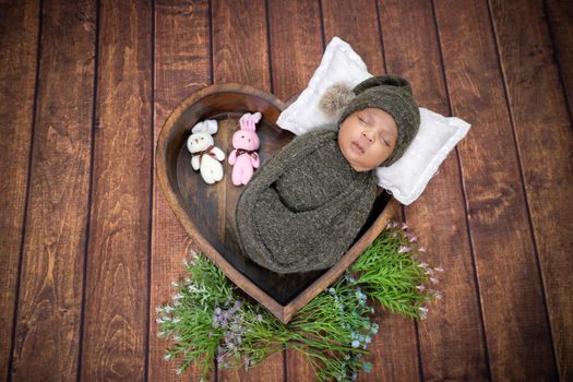 Sweet newborn baby wrapped in a cozy knit outfit, sleeping in a heart-shaped bowl with floral accents.