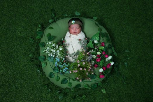 Peaceful newborn wrapped in white, nestled among vibrant flowers on a green backdrop.
