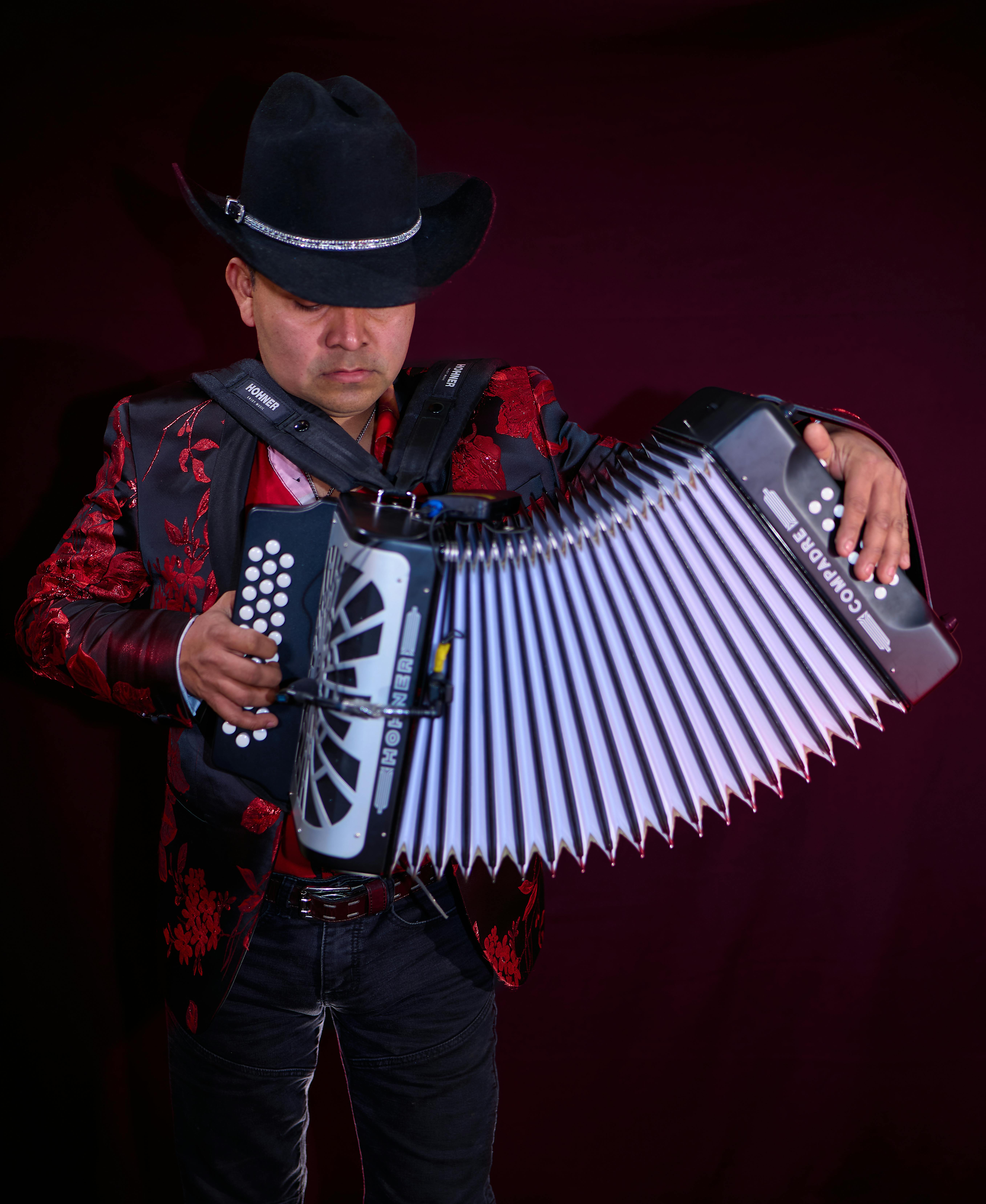 Musician in black hat and red jacket playing accordion with focus and passion.