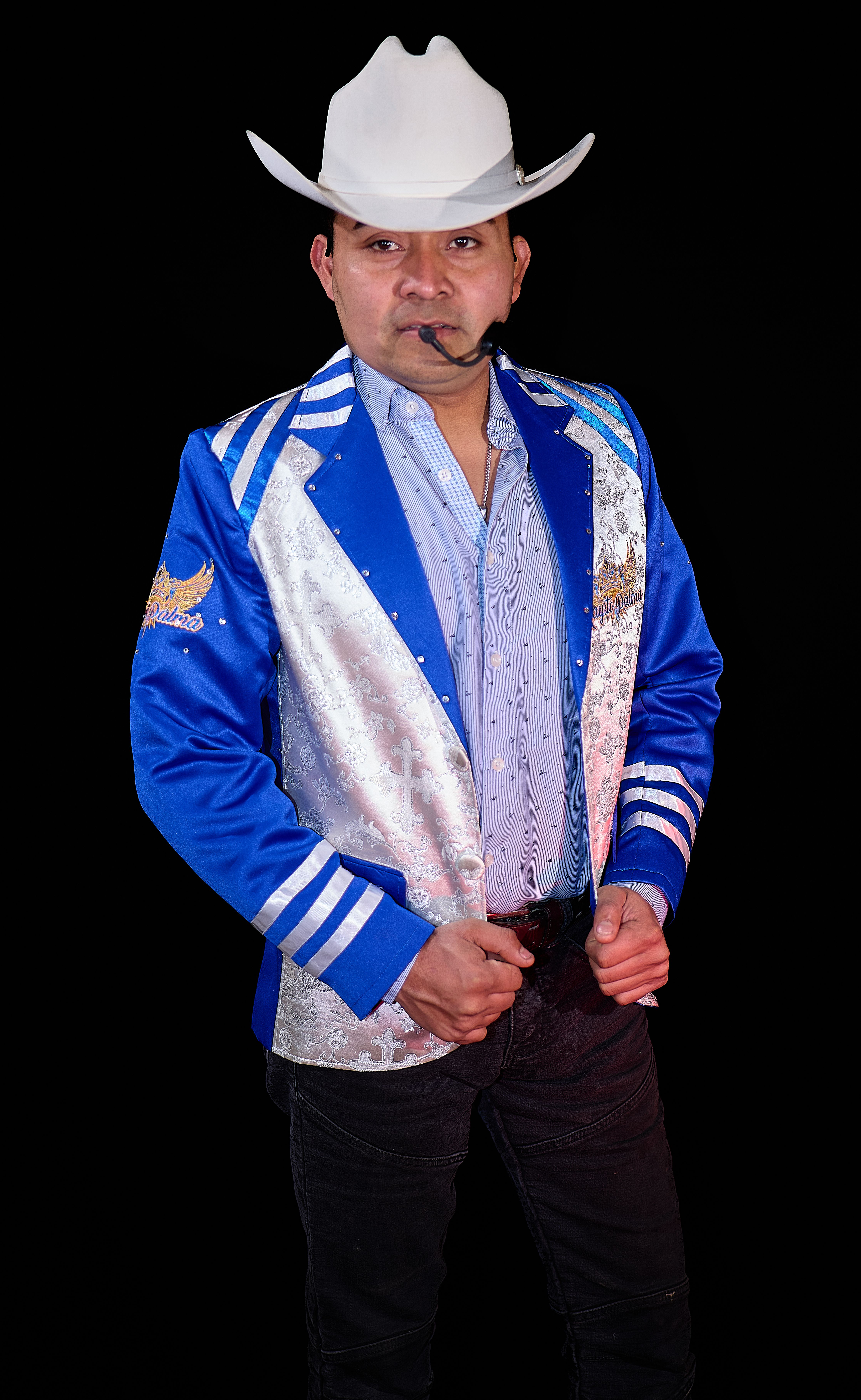 Man in blue jacket with white cowboy hat, black background, confident pose.