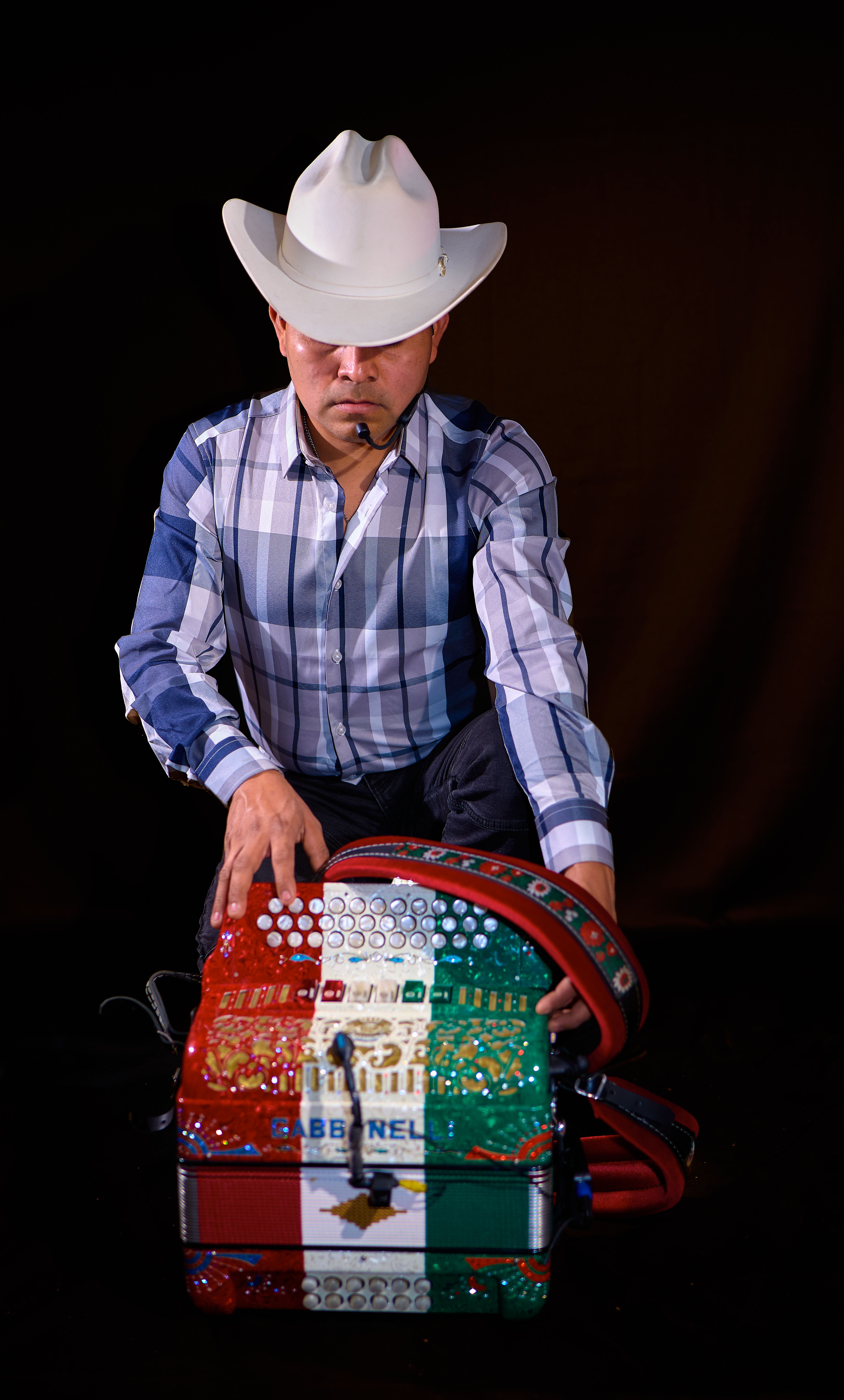 Man in a cowboy hat playing a multicolored accordion, indoor setting.