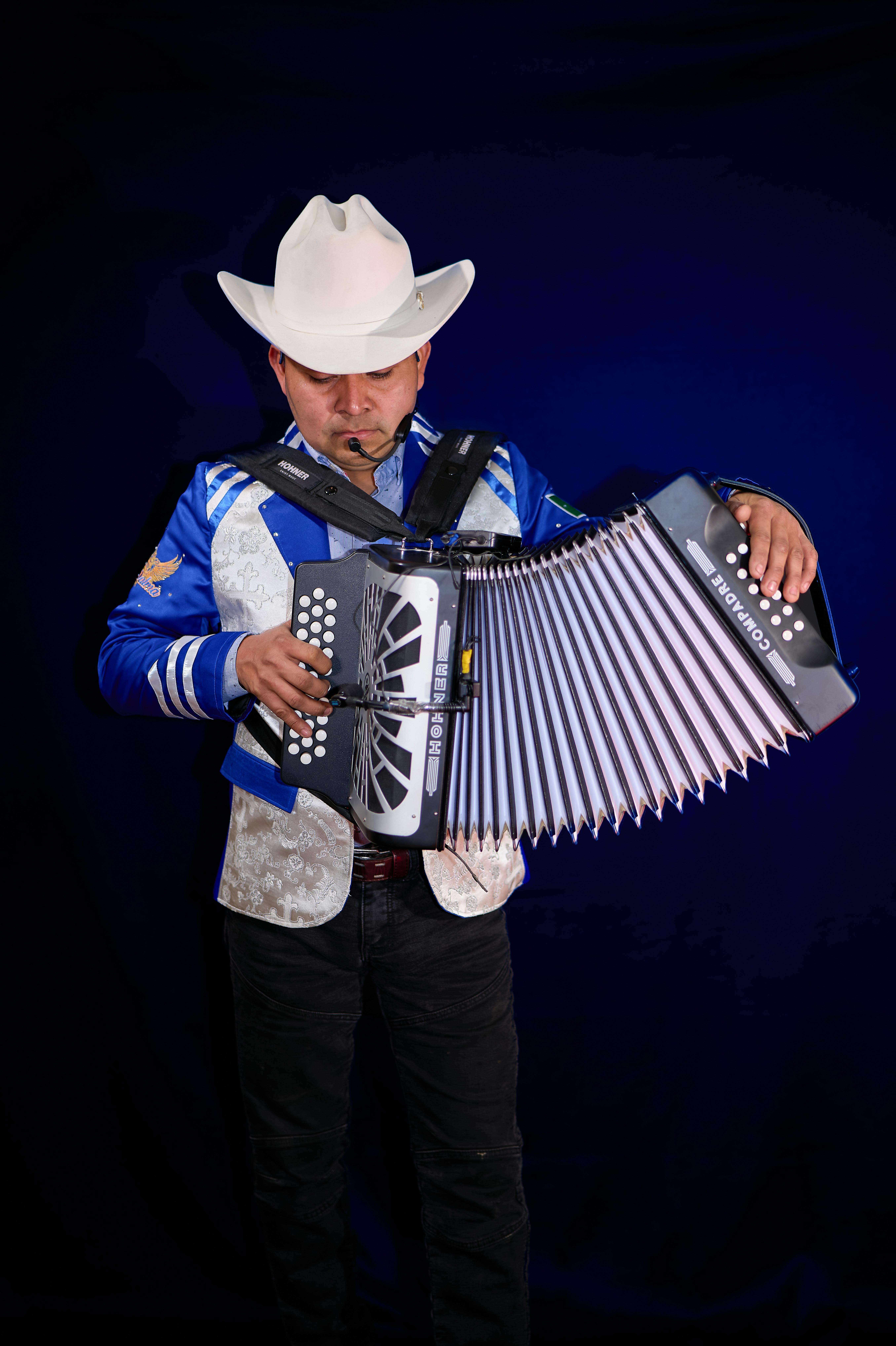 An adult male musician in traditional attire playing an accordion on stage under spotlight.