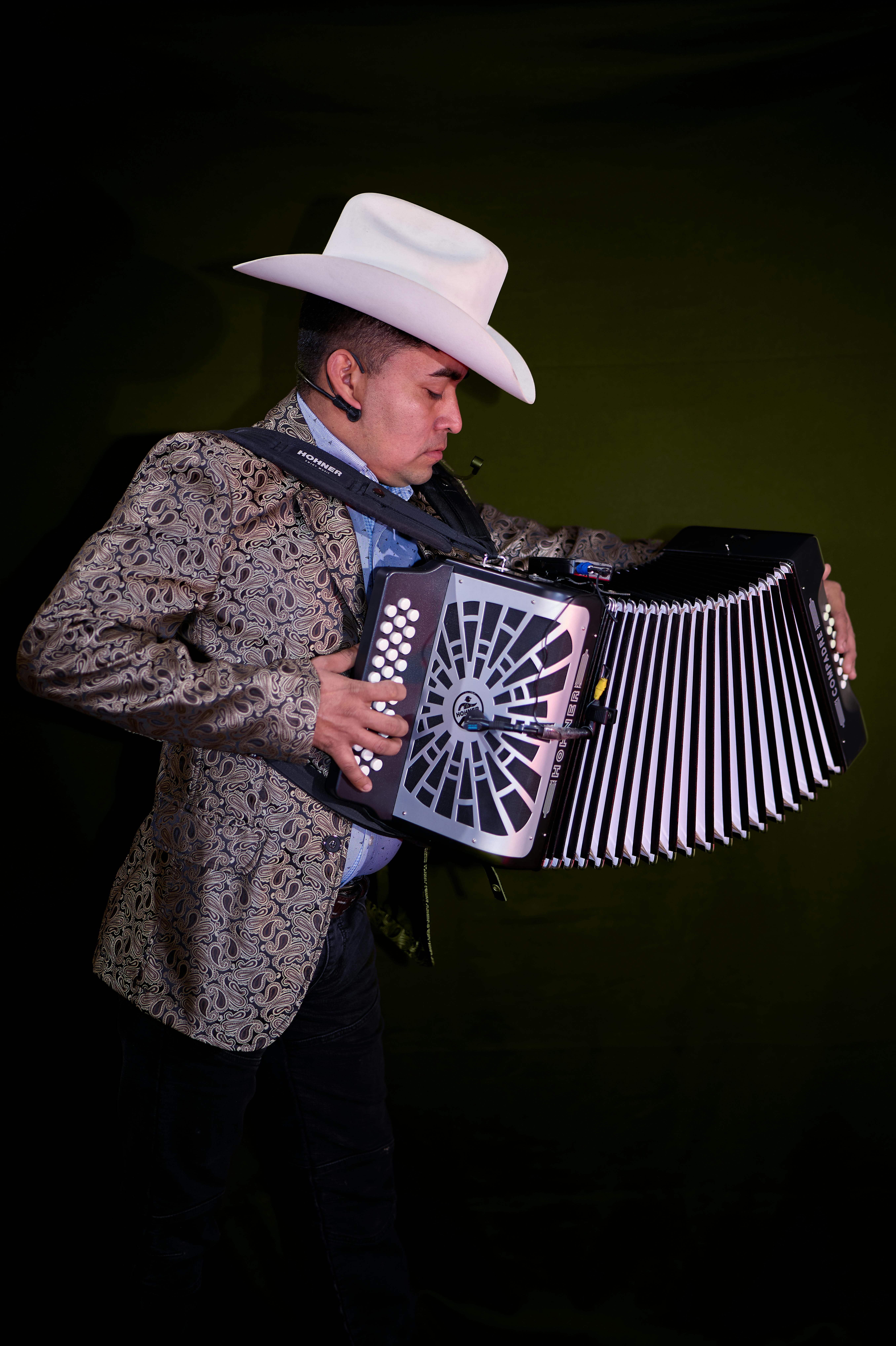 A man in a cowboy hat plays an accordion against a dark backdrop.
