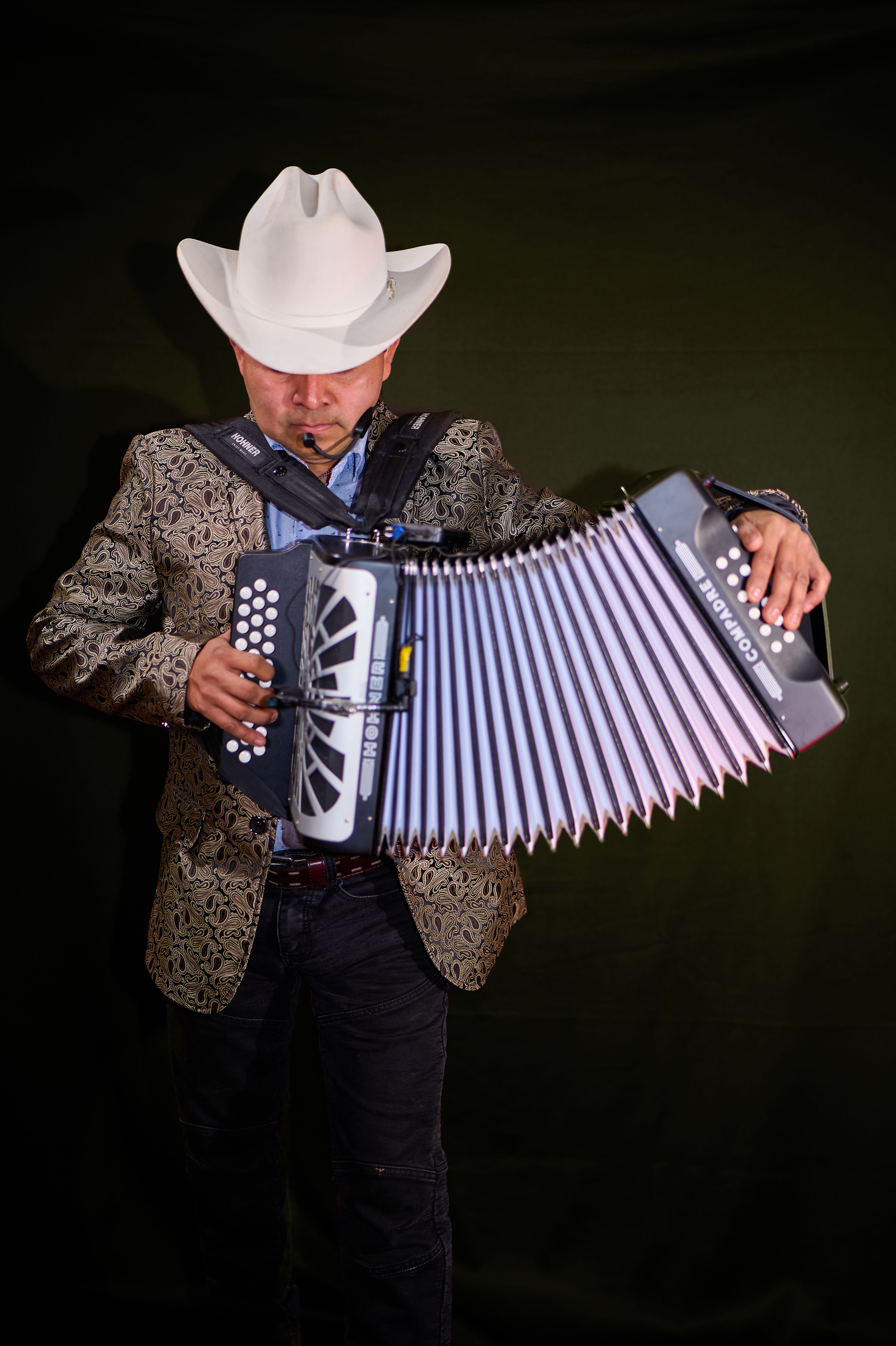 A man wearing a cowboy hat expertly plays an accordion against a dark background.
