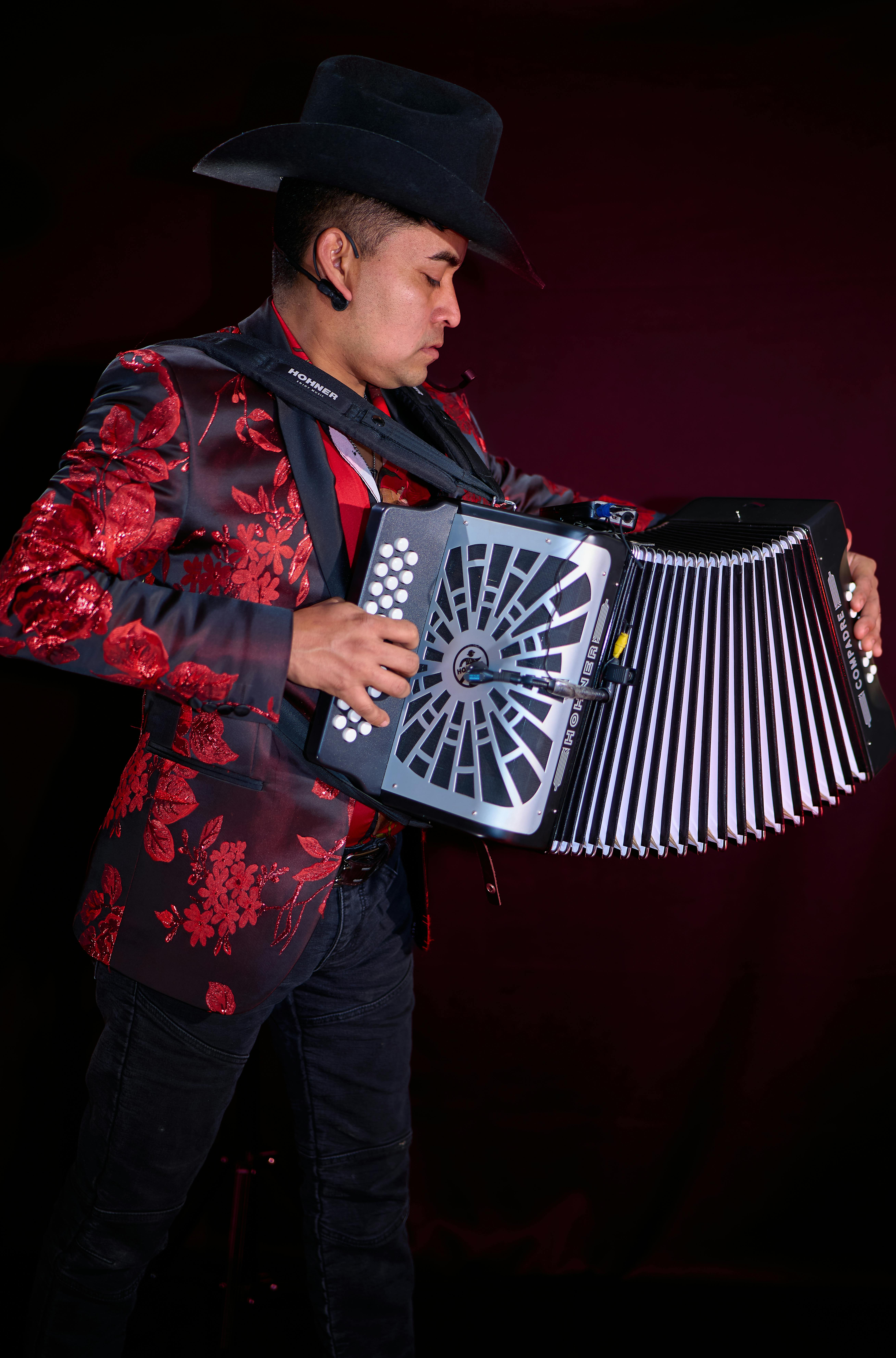 A man wearing a floral suit and cowboy hat plays an accordion passionately on stage. Musical performance concept.