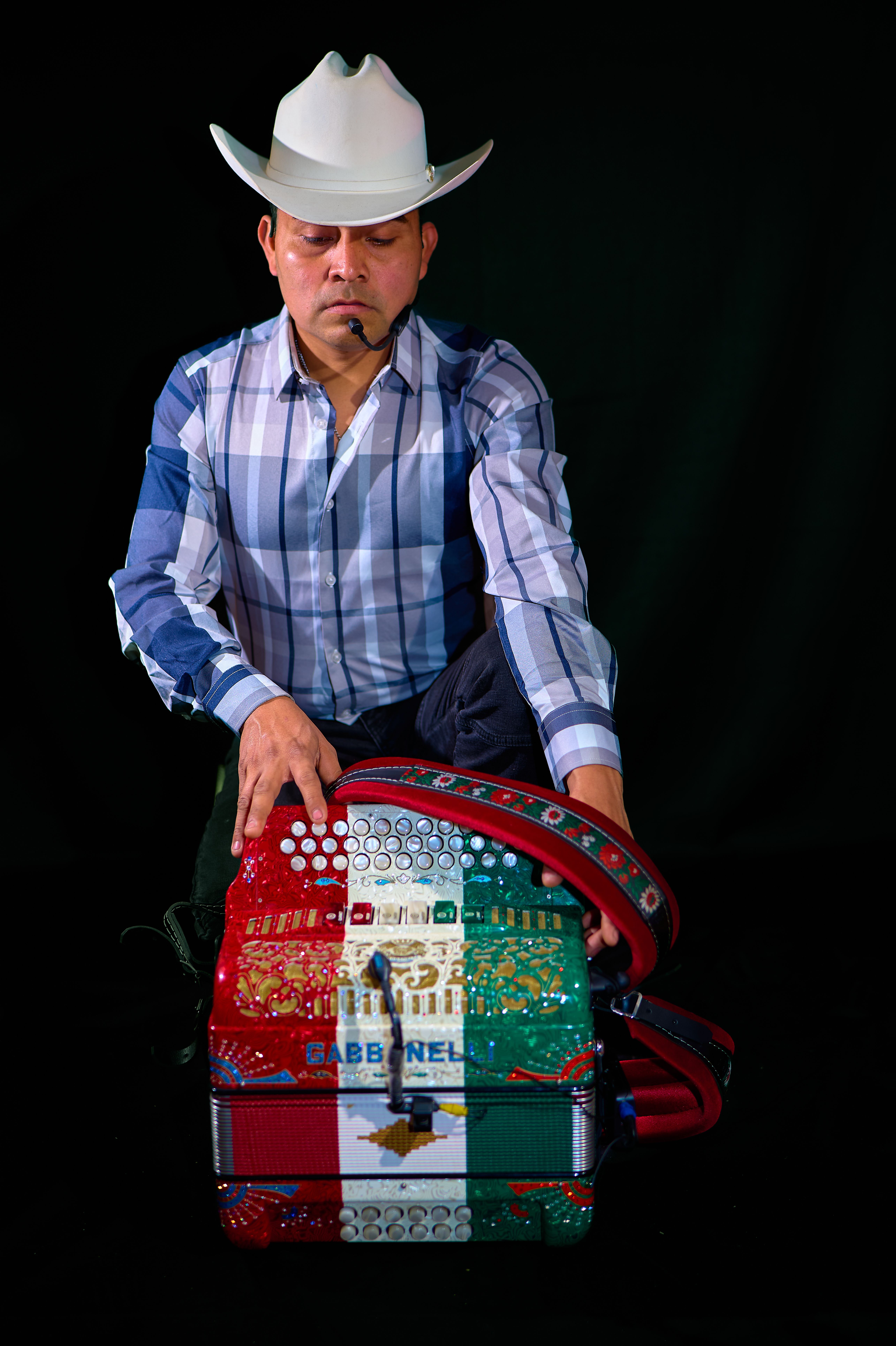 Man in cowboy hat playing a colorful Mexican-themed accordion on a dark background.