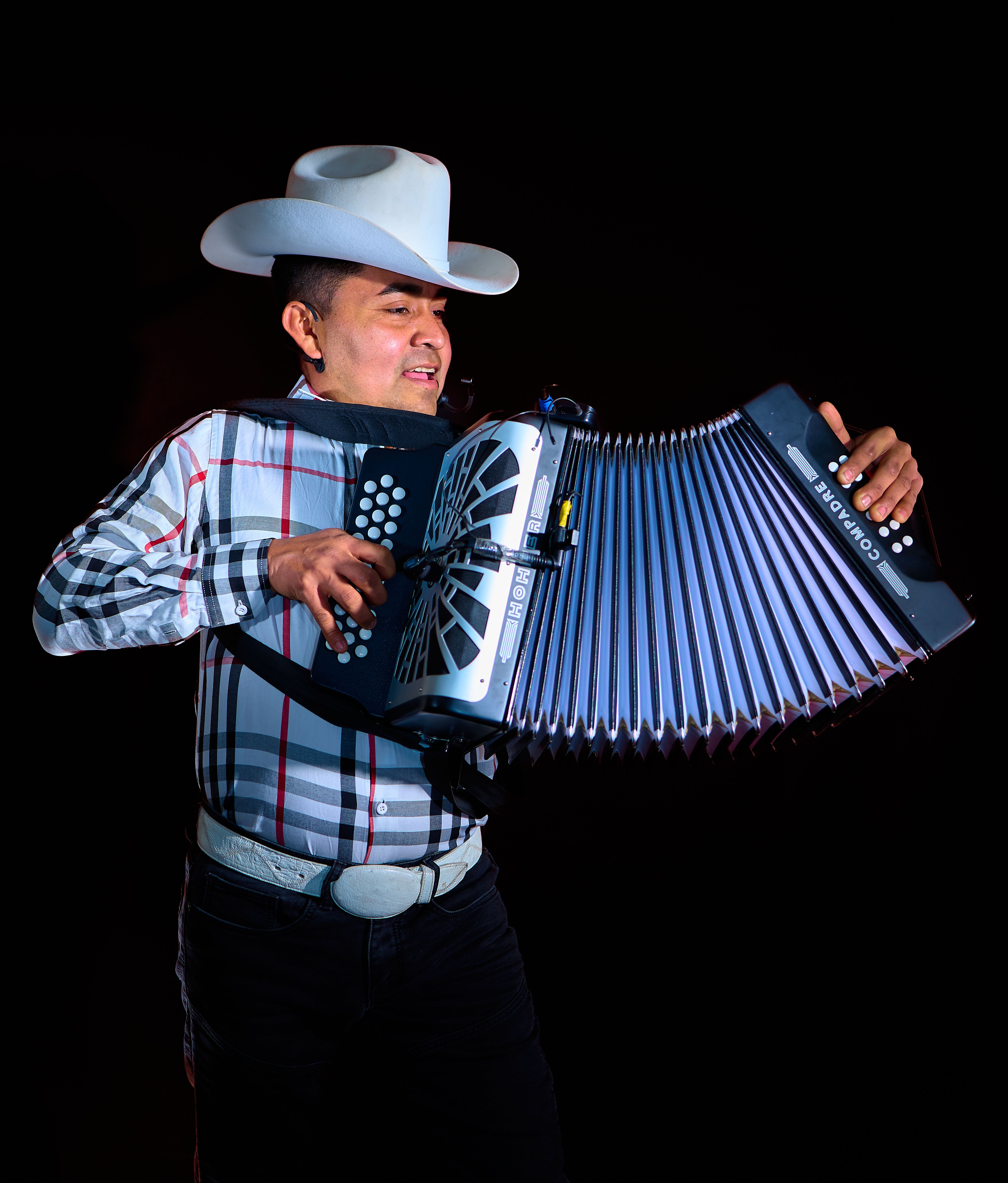 A man wearing a cowboy hat and plaid shirt passionately plays an accordion on stage.