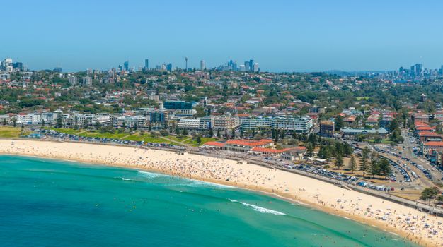 Capture the vibrant coastal scene of Bondi Beach in Sydney from above, showcasing city skyline and sandy shores.