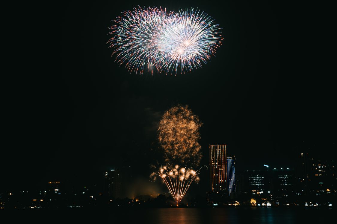 Free Dazzling fireworks illuminate the night sky over a cityscape, capturing festive celebration spirit. Stock Photo