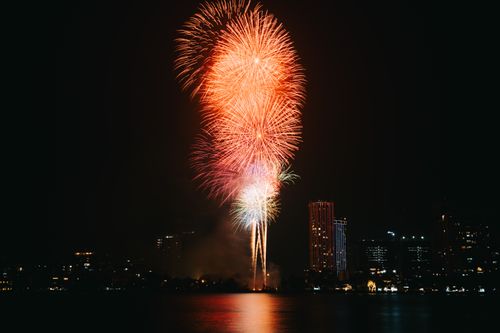 Free Vivid fireworks burst over a city skyline at night, reflecting on water below. Stock Photo