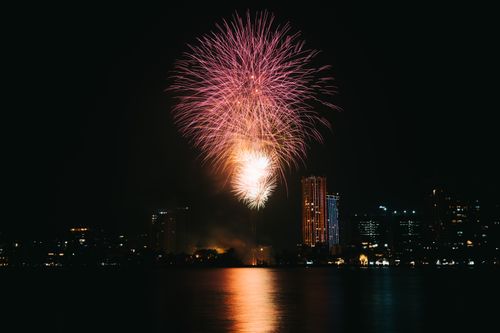 Free Dazzling fireworks illuminate the night sky over a bustling city skyline reflecting on the water. Stock Photo