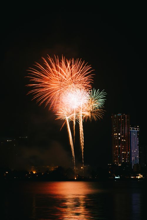 Free Vibrant fireworks illuminate the night sky over a city skyline, reflecting on the water below. Stock Photo