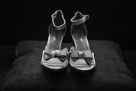 一张黑白照片展示了黑色枕头上优雅的蝴蝶结高跟凉鞋，彰显时尚风格