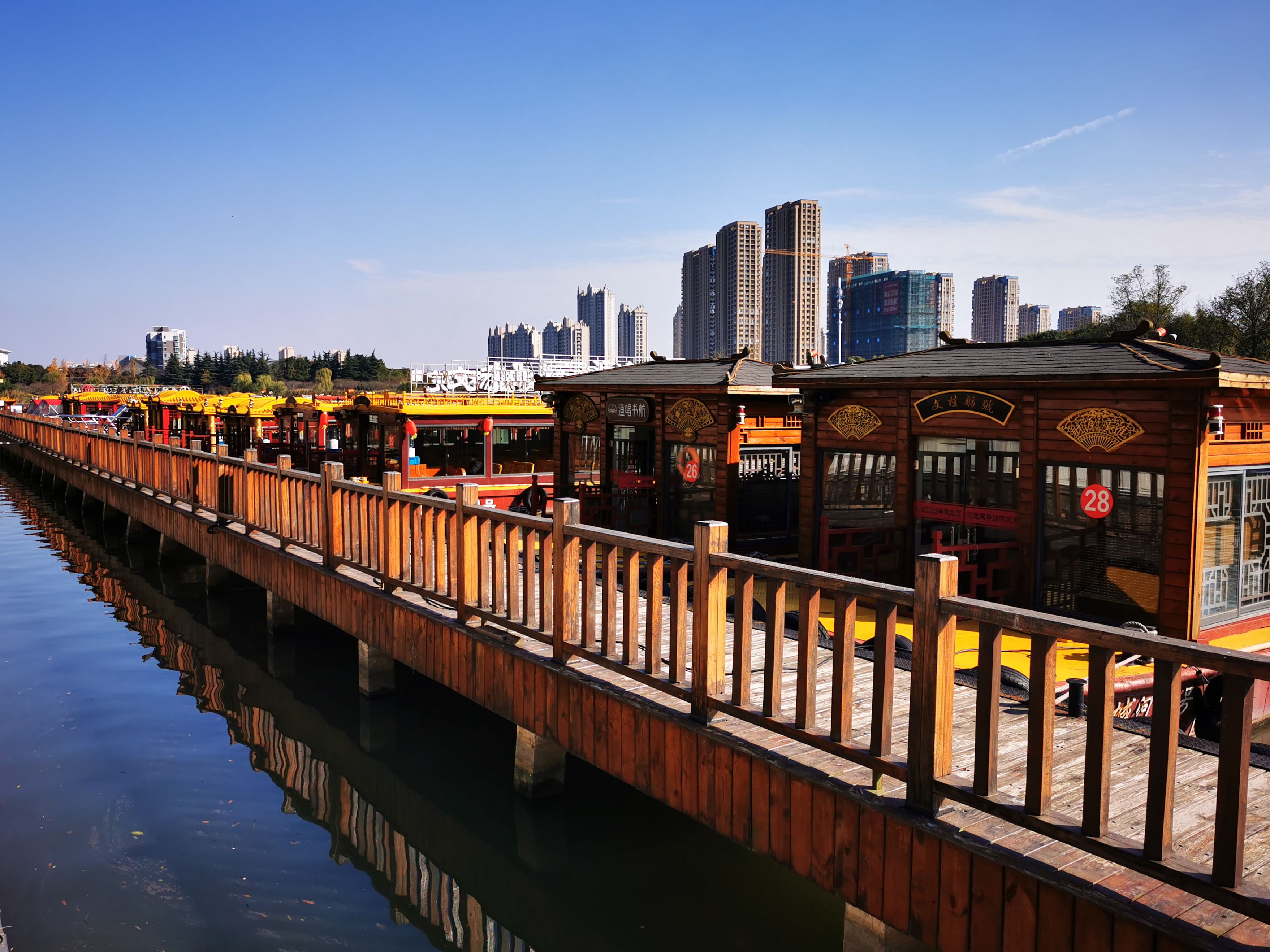 Free Wooden boardwalk on waterfront with traditional boats and modern urban skyline in the background. Stock Photo