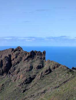 Stunning view of rugged mountain cliffs against the backdrop of a clear blue ocean under a bright sky.