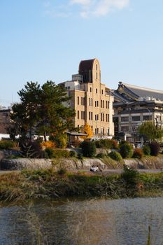 Scenic view of a historic building by a river in autumn, showcasing vibrant colors.