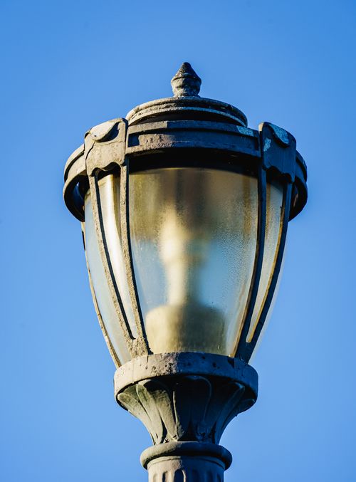 Free Close-up of an ornate street lamp with a Victorian design set against a bright blue sky. Stock Photo