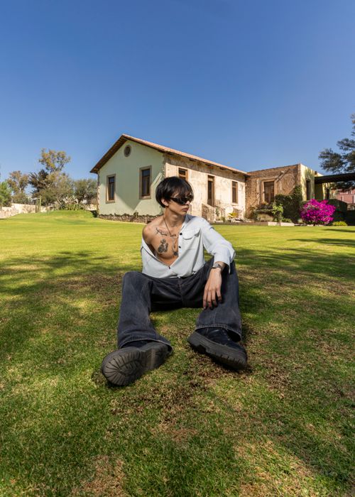 Free Young man in casual attire sitting on grass near traditional building in Ibarrilla, Guanajuato, Mexico. Stock Photo