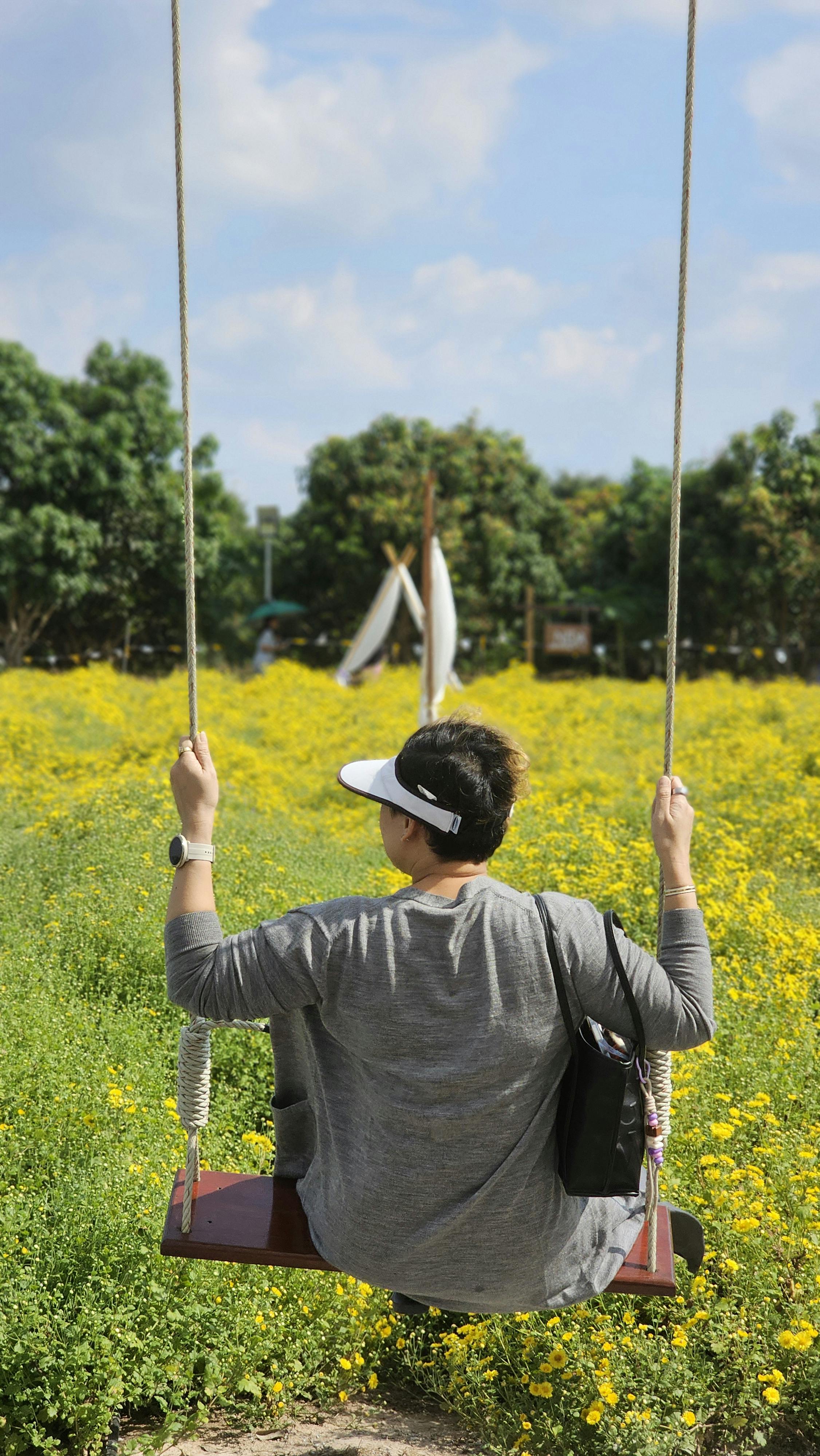Person enjoying a sunny day on a swing in a vibrant yellow flower field outdoors.
