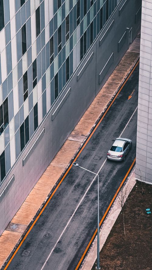 Free Aerial shot of a car driving on a narrow street between tall modern buildings. Stock Photo