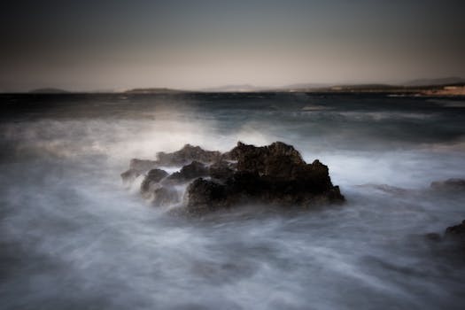 Dramatic seascape with rugged rocks and misty waves under twilight skies.