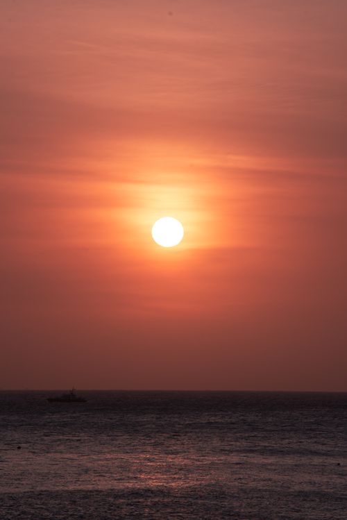 Free Serene sunset casting vibrant hues over calm ocean waves with a distant boat. Stock Photo