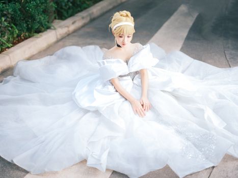 Elegant bride sitting on the ground in a flowy white gown, captured outdoors.