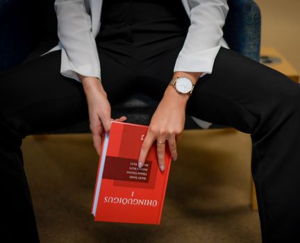 Close-up of a woman in a library holding a red book, emphasizing study and education.
