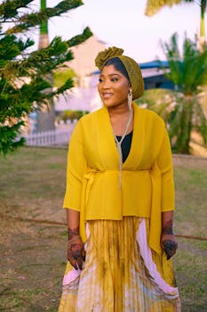 A woman in a stylish yellow dress and headwrap standing outdoors with a smile.
