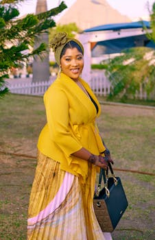Smiling woman in vibrant yellow outfit posing outdoors with patterned skirt and handbag.