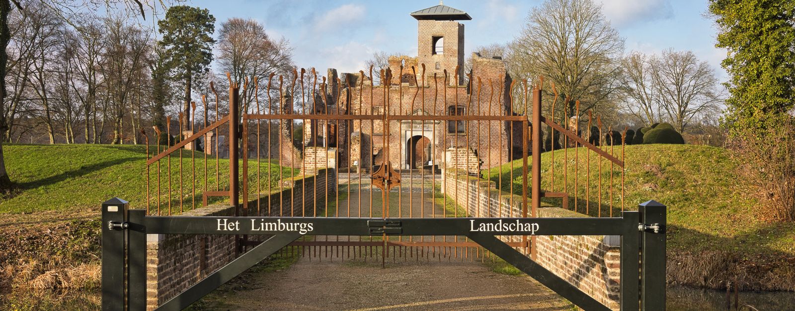 View of a historic castle gate surrounded by lush landscape under a clear sky.