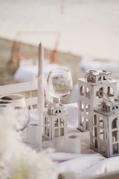 A beautiful, elegant table setup at a beachfront with decorative lanterns and glassware.