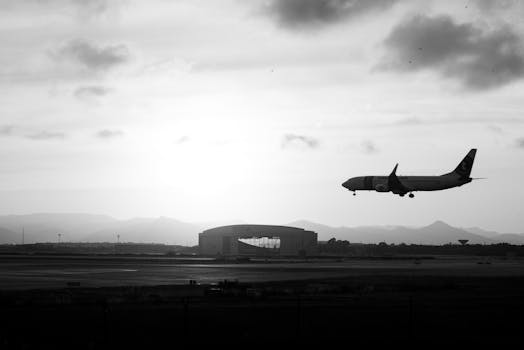 A silhouette of an airplane landing against a dramatic sunset, with mountains in the background.
