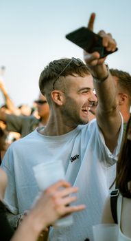 A young man enthusiastically celebrates with friends at an outdoor music festival, sharing a joyful moment.