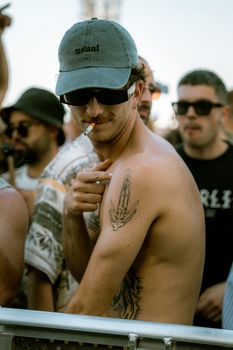 Man enjoying a sunny outdoor festival, showcasing tattoos and relaxed fashion style.