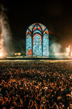 A lively crowd at a night concert featuring an impressive stained glass backdrop and dynamic lighting.