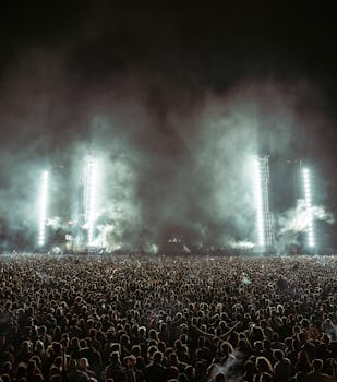 Captivating shot of a massive crowd enjoying a music festival under bright stage lights at night.