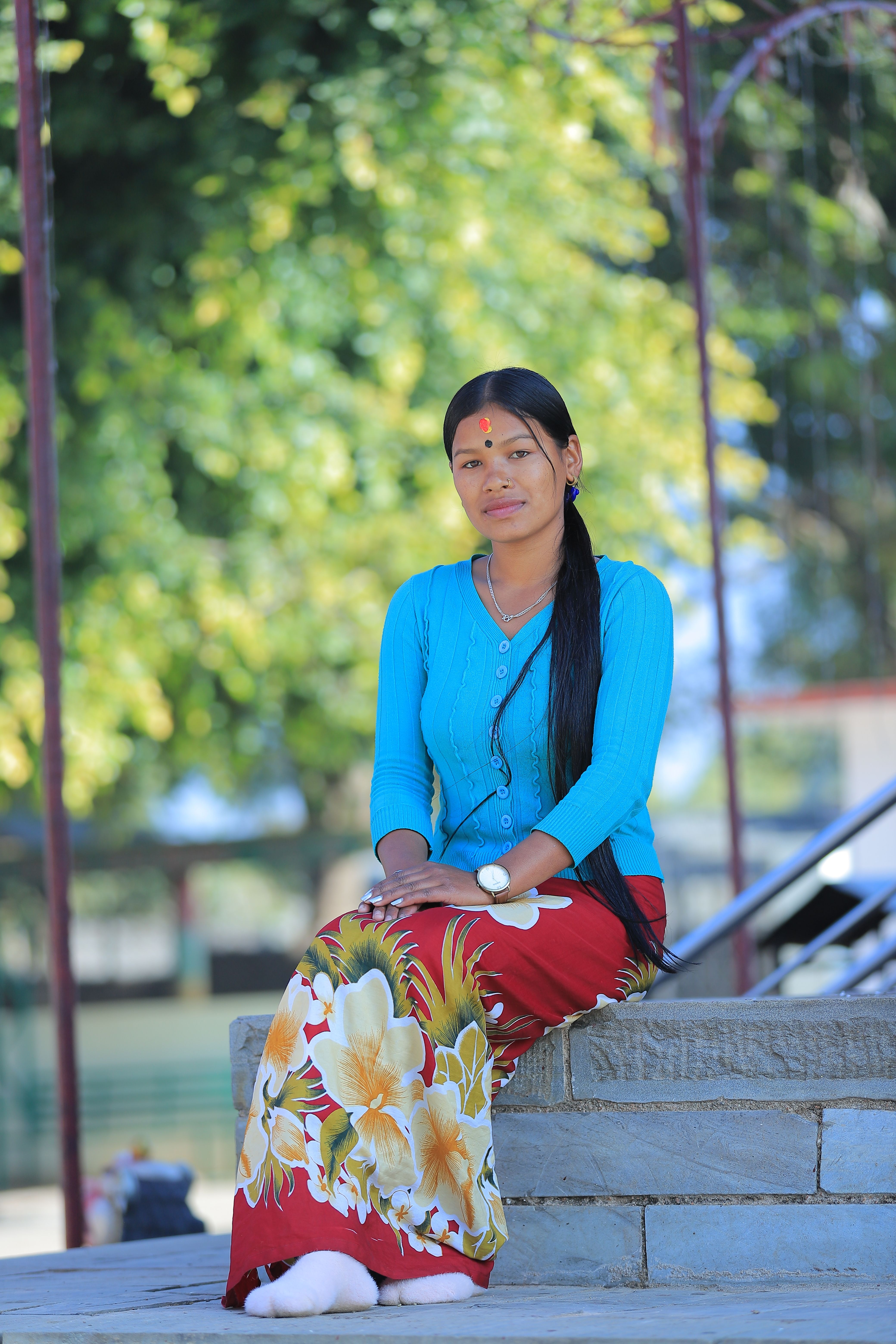 Woman with long hair in traditional outfit sitting outside on a sunny day.