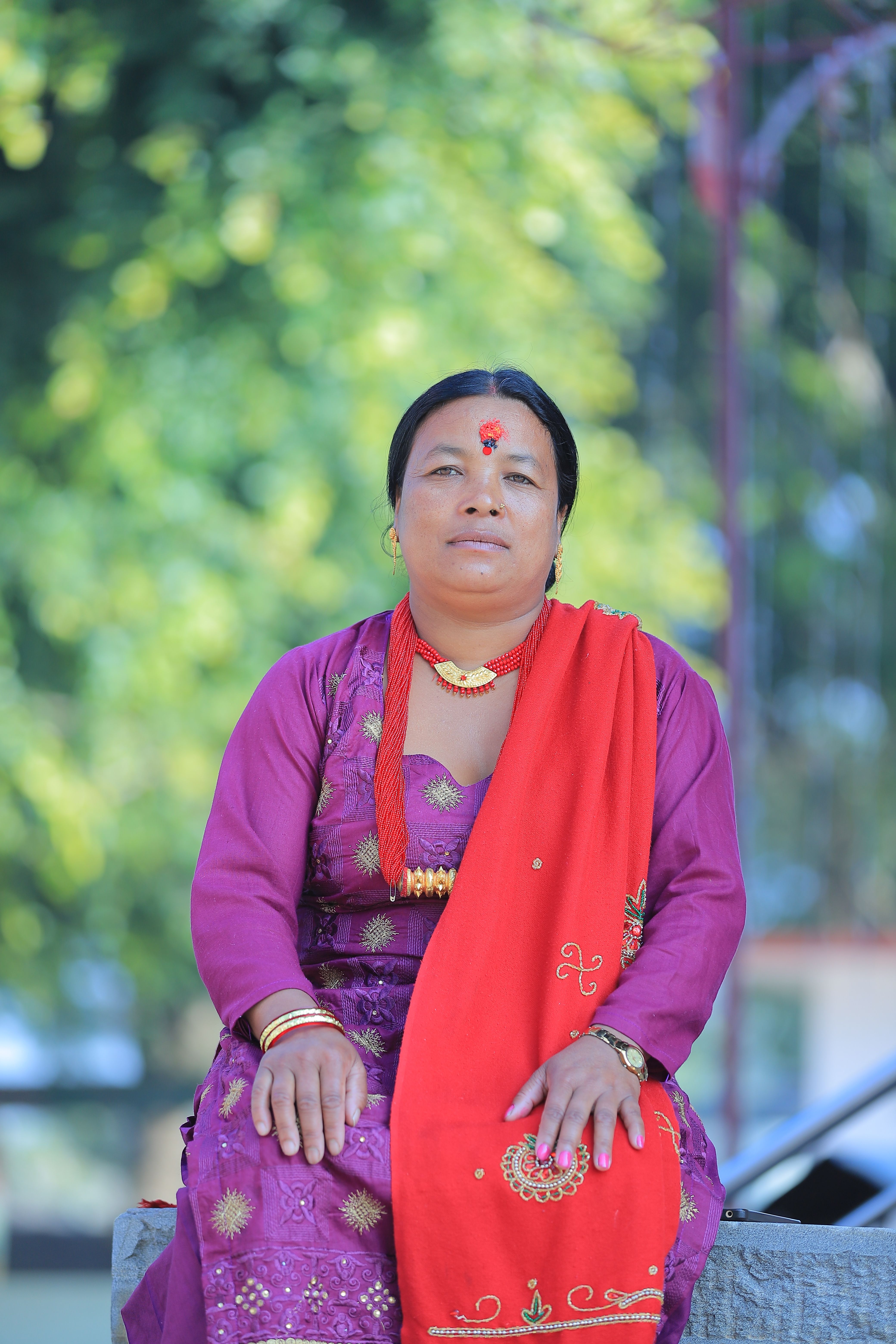 A woman in traditional vibrant attire poses outdoors with a calm expression.