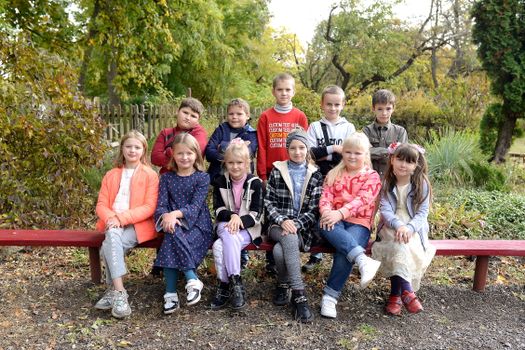 Happy group of kids sitting on a bench in a park during fall, enjoying a sunny day.