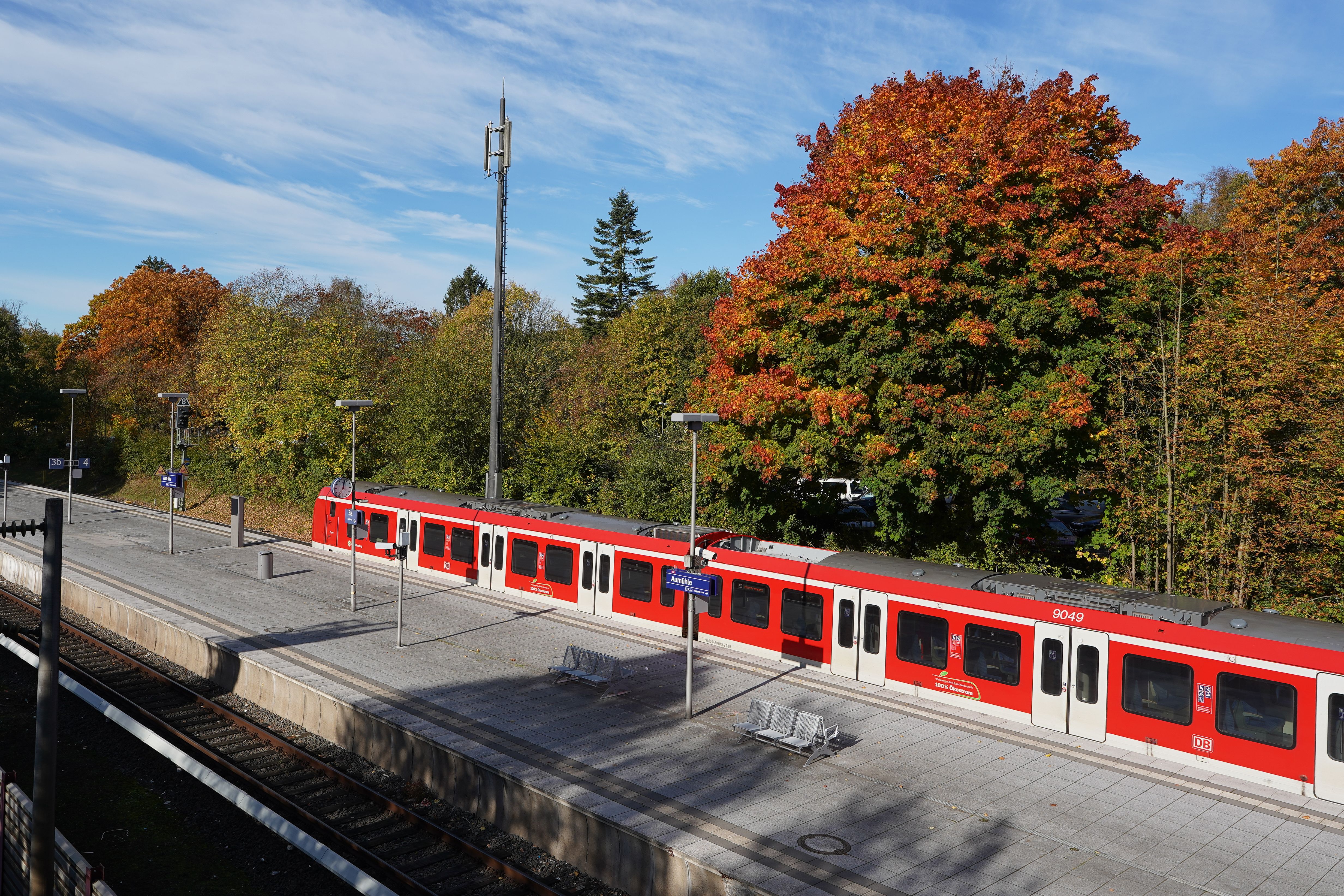 Scenic view of Aumühle train station with red train and vibrant autumn foliage.