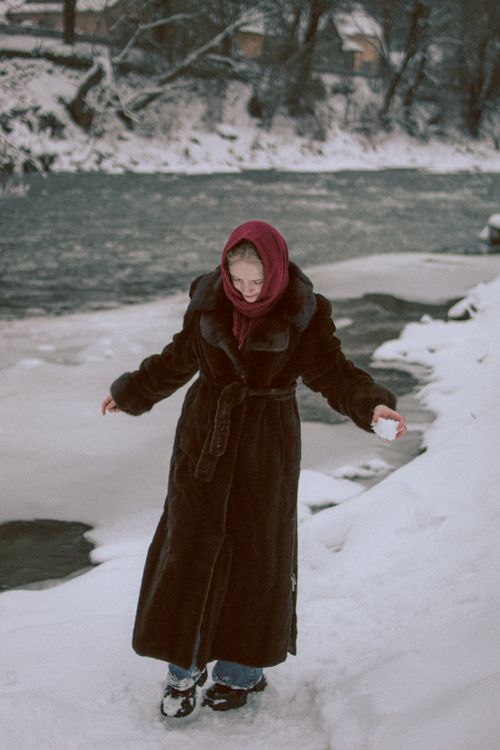 Free Woman in fur coat and red scarf by a snowy riverbank, enjoying winter outdoors. Stock Photo