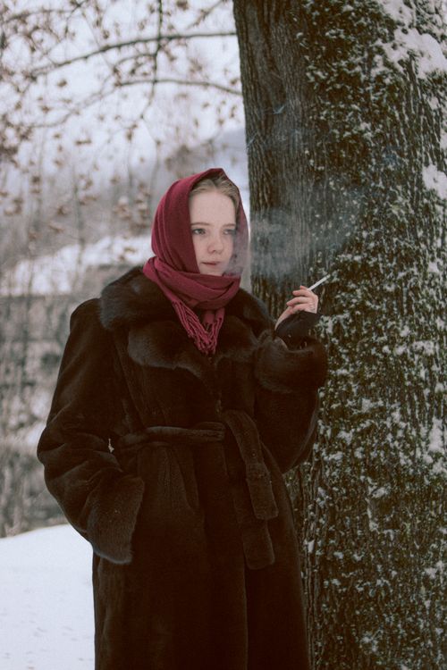 Free A woman wearing a fur coat and headscarf stands outdoors smoking in winter. Stock Photo