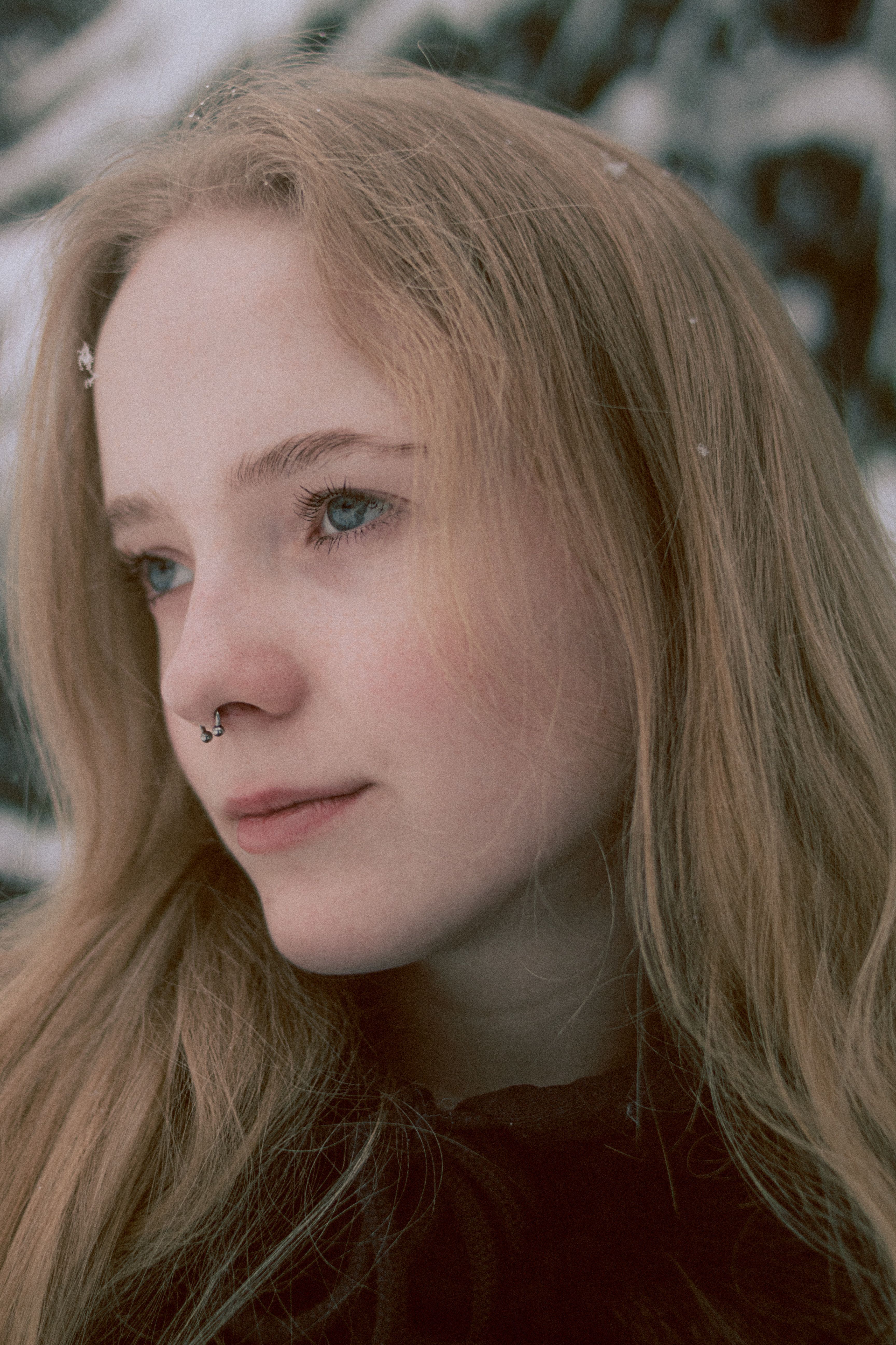 Portrait of a young woman with piercings and long hair in a snowy winter setting.