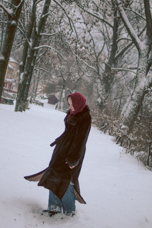 Free Woman in a long coat and headscarf walking through a snowy park with bare trees. Stock Photo