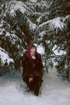 A woman wearing a red headscarf sits among snow-covered evergreen trees.