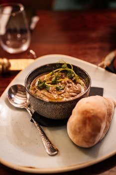 A comforting bowl of warm lentil soup garnished with herbs, served with fresh bread on a rustic wooden table.
