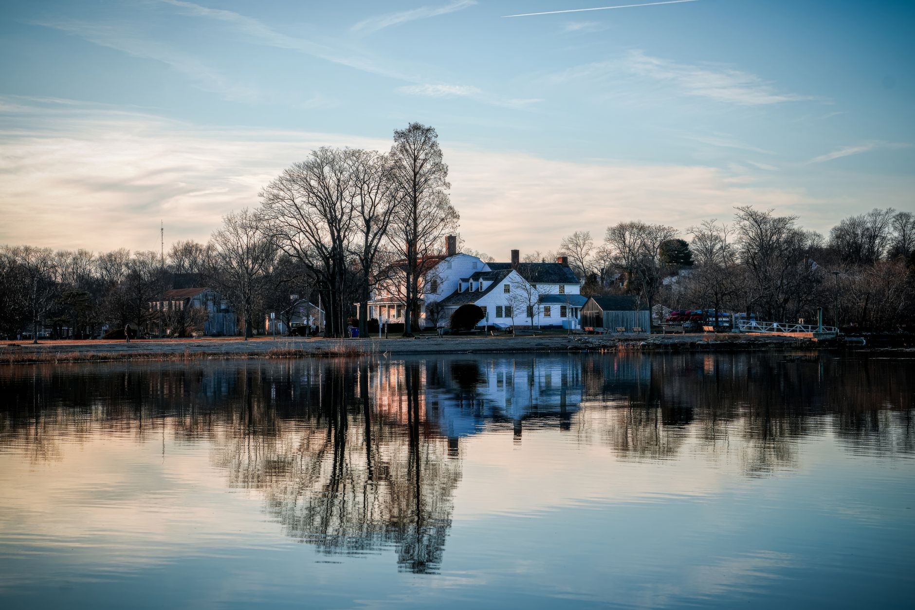Serene reflection of a historic lakefront house surrounded by bare trees at dusk.