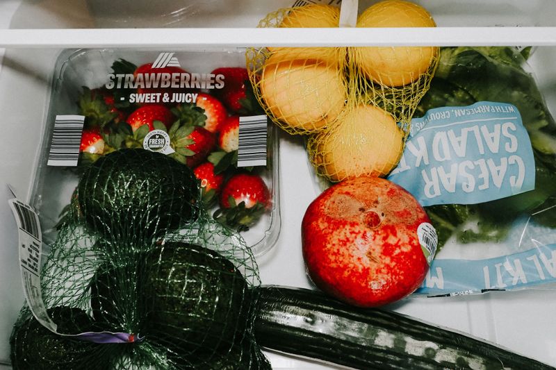 A variety of fresh fruits and vegetables including avocados, lemons, strawberries, and lettuce in a fridge drawer.