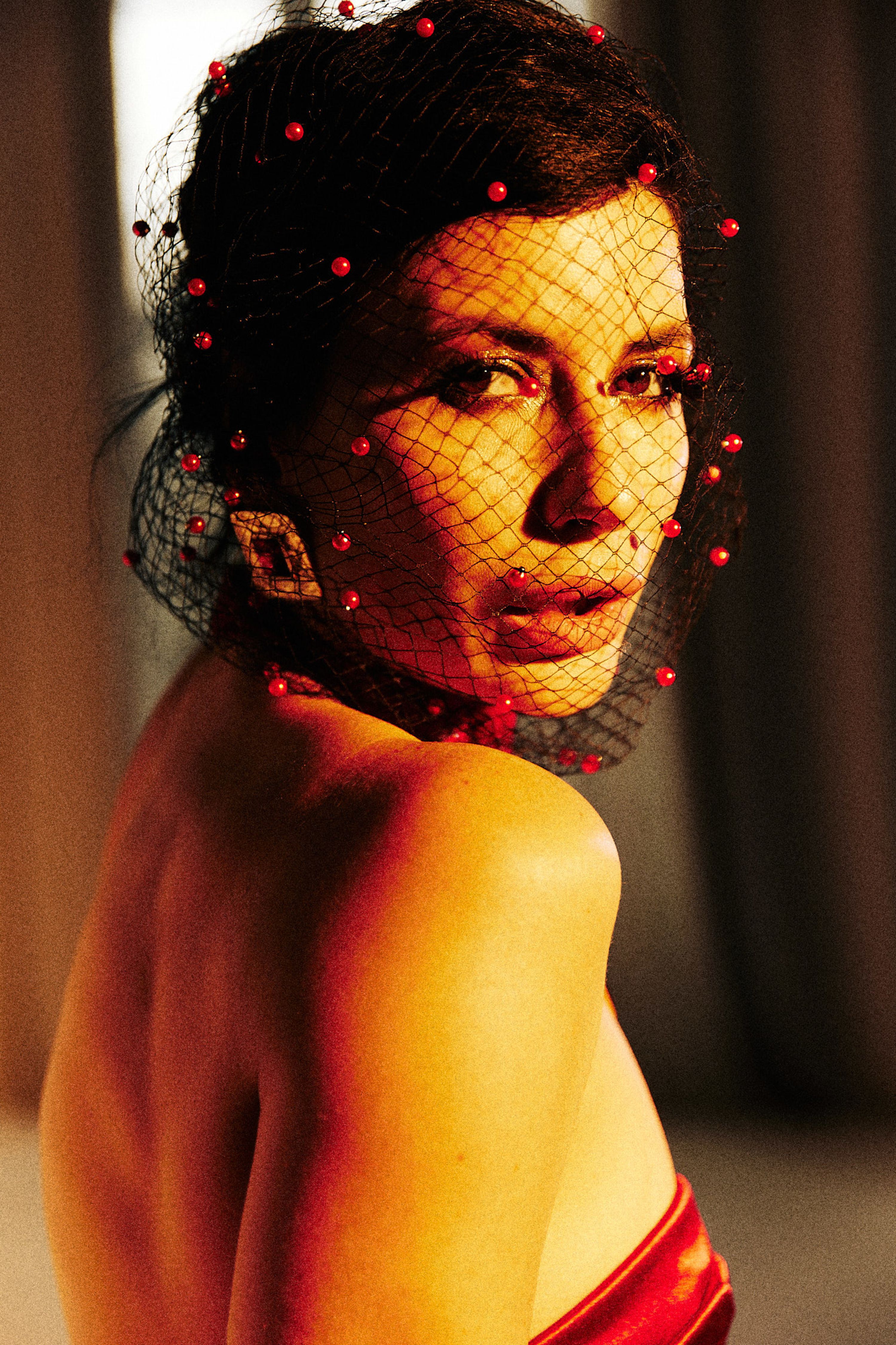 Portrait of a woman in a red dress and decorative veil adorned with beads, exuding elegance and mystery.